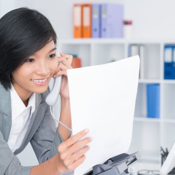 sfax online fax service cost features happy woman on the phone in office holding white papers in hand computer and folders in the background